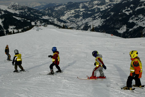 Skikurs: Skilehrer fährt voraus, kleine Kinder fahren im Schneepflug hinten nach.