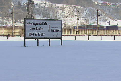 Schild eines Immobilienmaklers auf verschneiter Wiese neben der Eisenbahn
