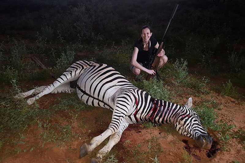 Jägerin posiert mit erlegtem Zebra und Gewehr in Südafrika