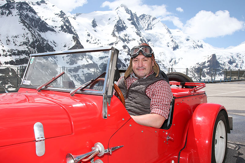 Rudi Roubinek in Oldtimer Cabrio auf der Franz Josefs Höhe an der Großglockner Hochalpenstraße mit Blick auf den Glockner