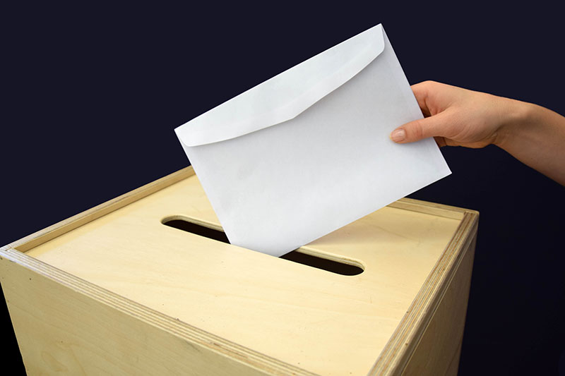 Umschlag wird in Wahlurne geworfen