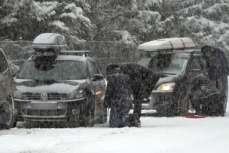 Urlauber legen Schneeketten bei Autos im Schneetreiben an
